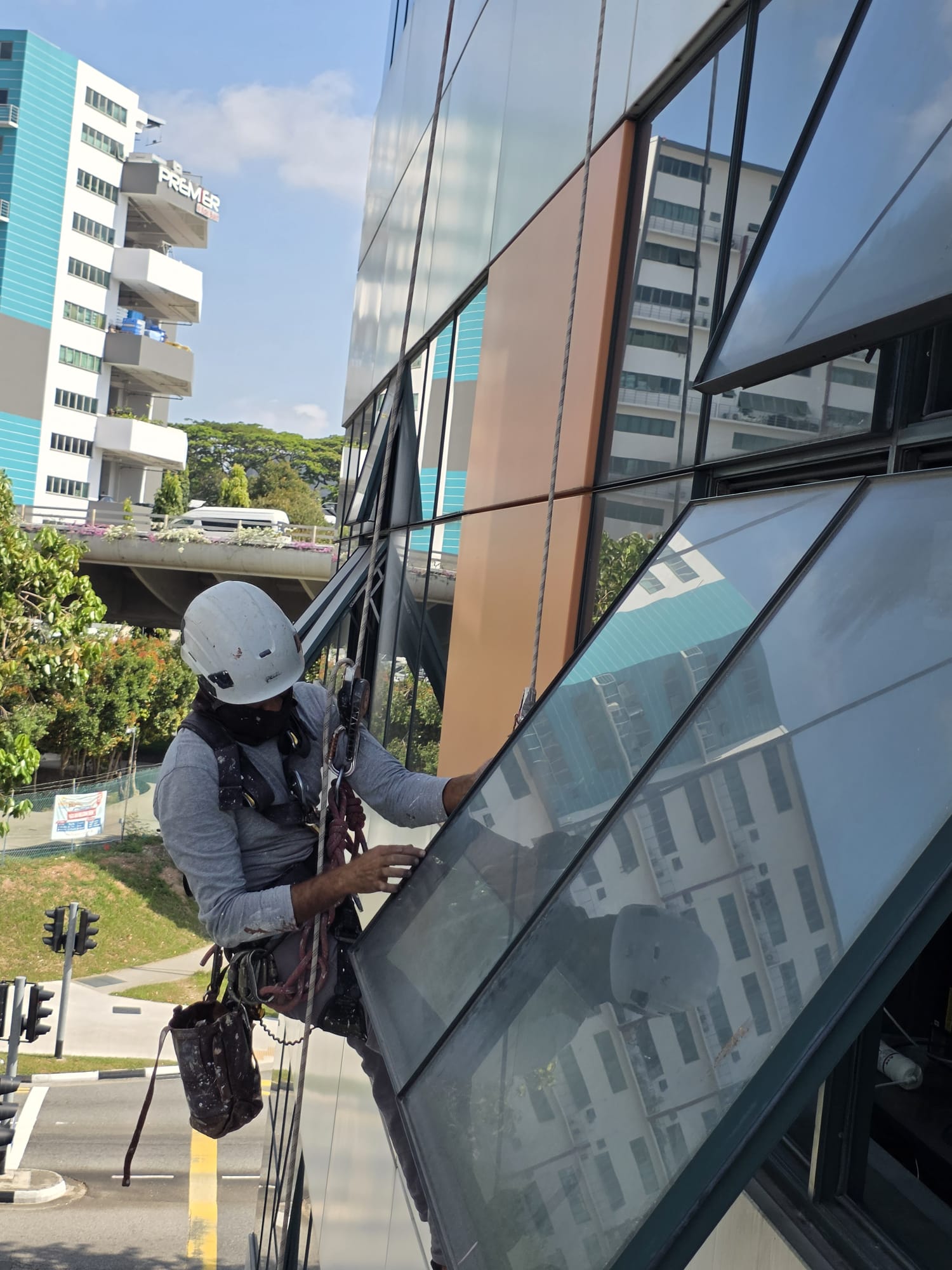 Rope-access worker inspecting beside a window at Kaki Bukit View