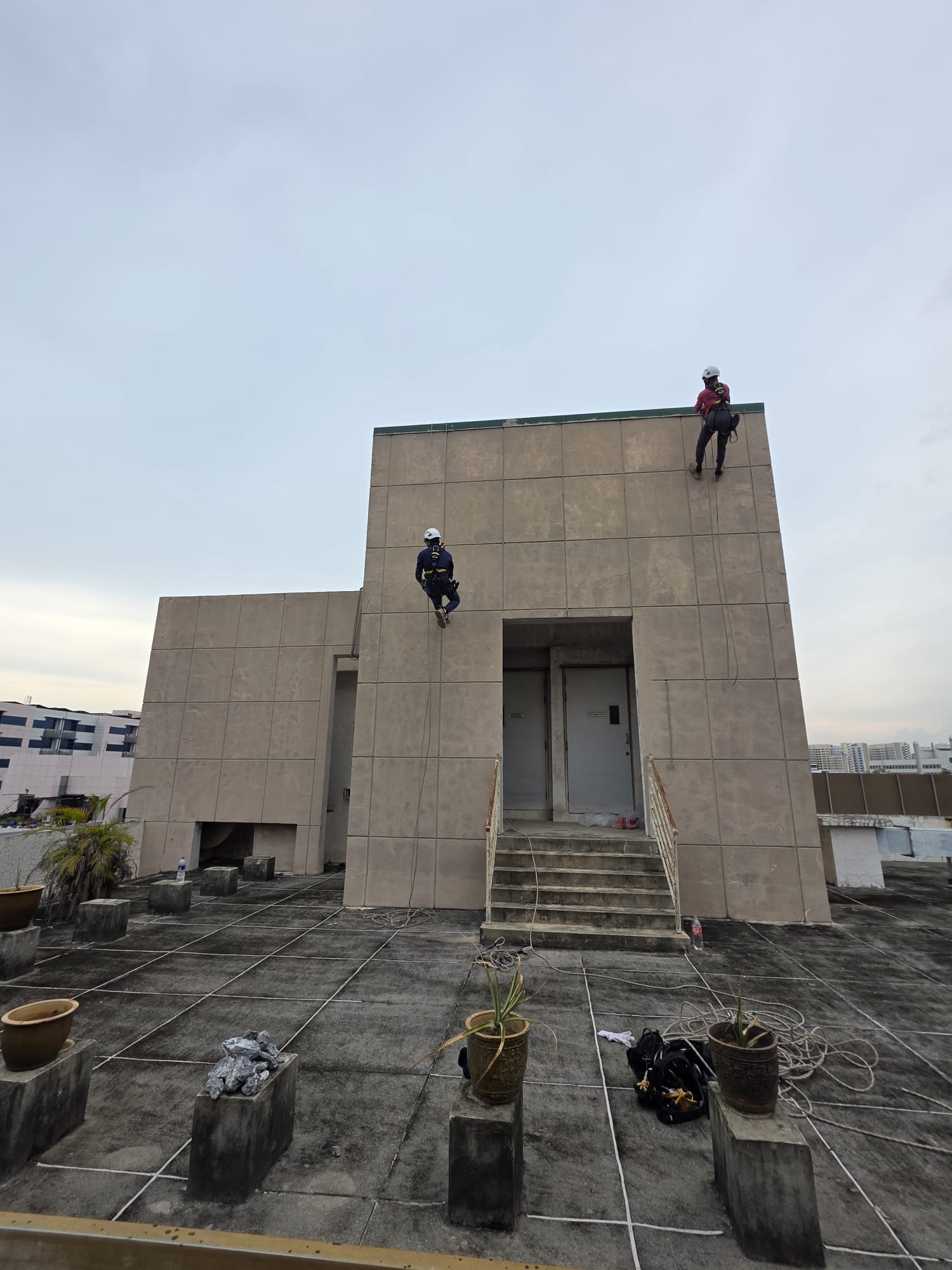 Two rope-access workers beside the upper facade structure at Ubi Crescent